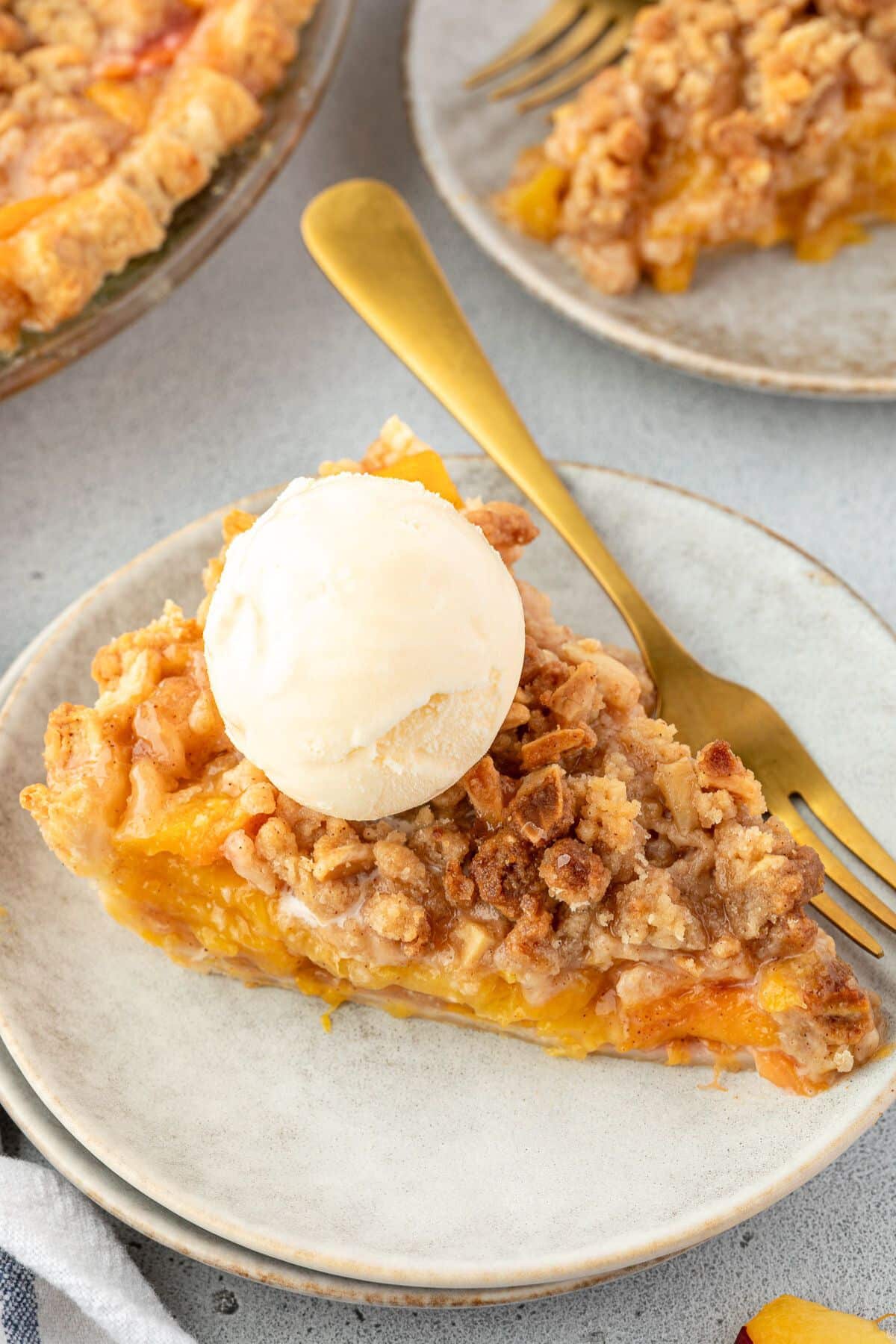 A slice of peach pie with a scoop of vanilla ice cream on a plate and a gold fork.