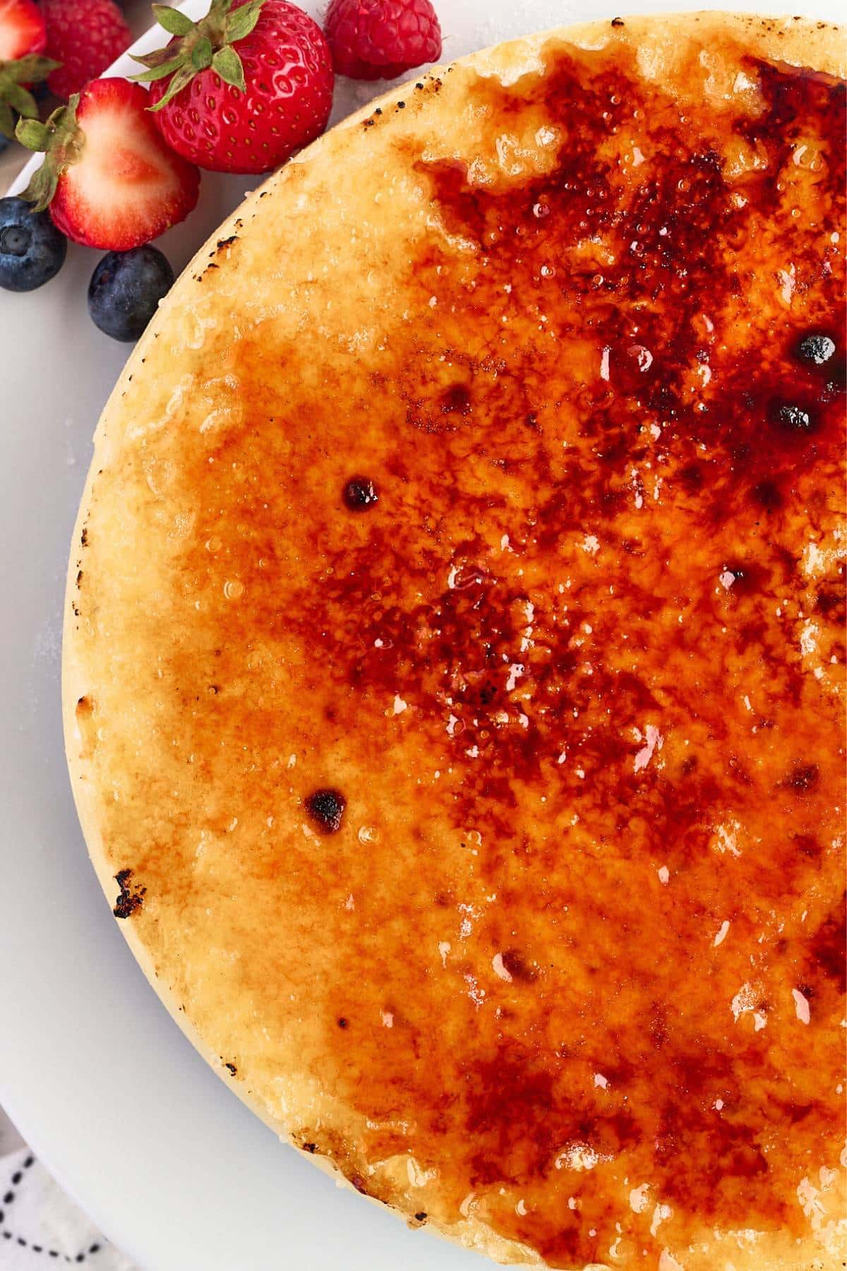 Close-up of a caramelized crème brûlée cheesecake topped with berries on the side.