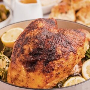 Roasted turkey breast with crispy skin, surrounded by lemon slices and herbs in a pan.