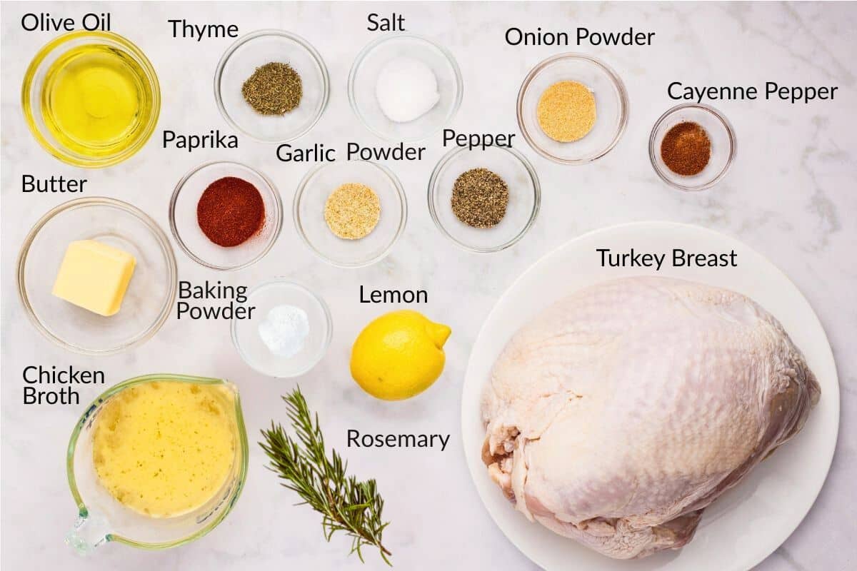 Ingredients for cooking turkey breast, including spices, olive oil, lemon, broth, and fresh rosemary on a countertop.