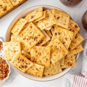 A bowl of seasoned square crackers topped with spices, viewed from above.
