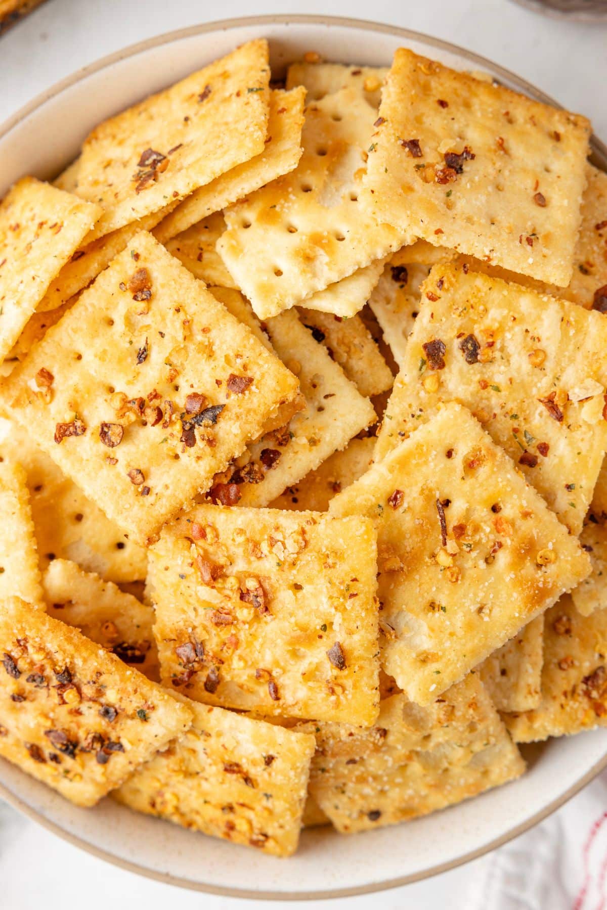 Bowl filled with seasoned, square crackers topped with visible herbs and spices.