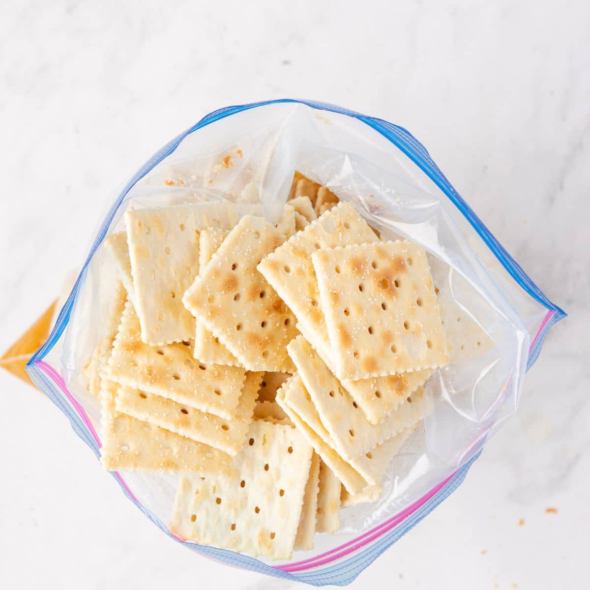 Saltine crackers in a resealable plastic bag, viewed from above on a white surface.
