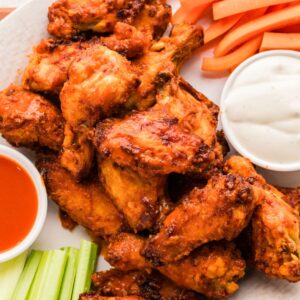 Plate of buffalo chicken wings with celery, carrot sticks, ranch dip, and hot sauce on the side.