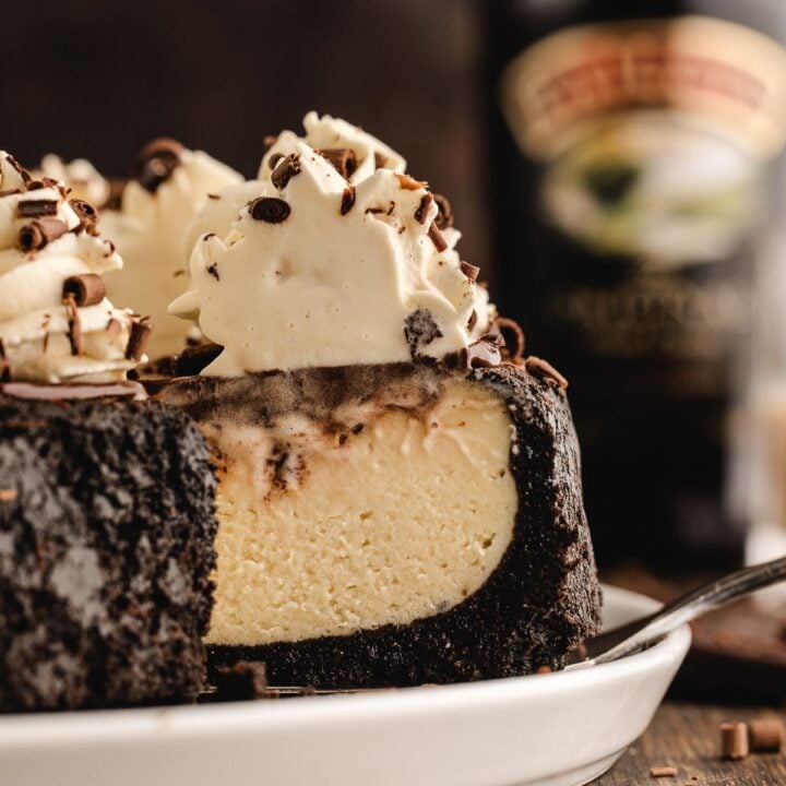 A creamy cheesecake with chocolate crust and whipped topping, served on a white plate with a slice removed.