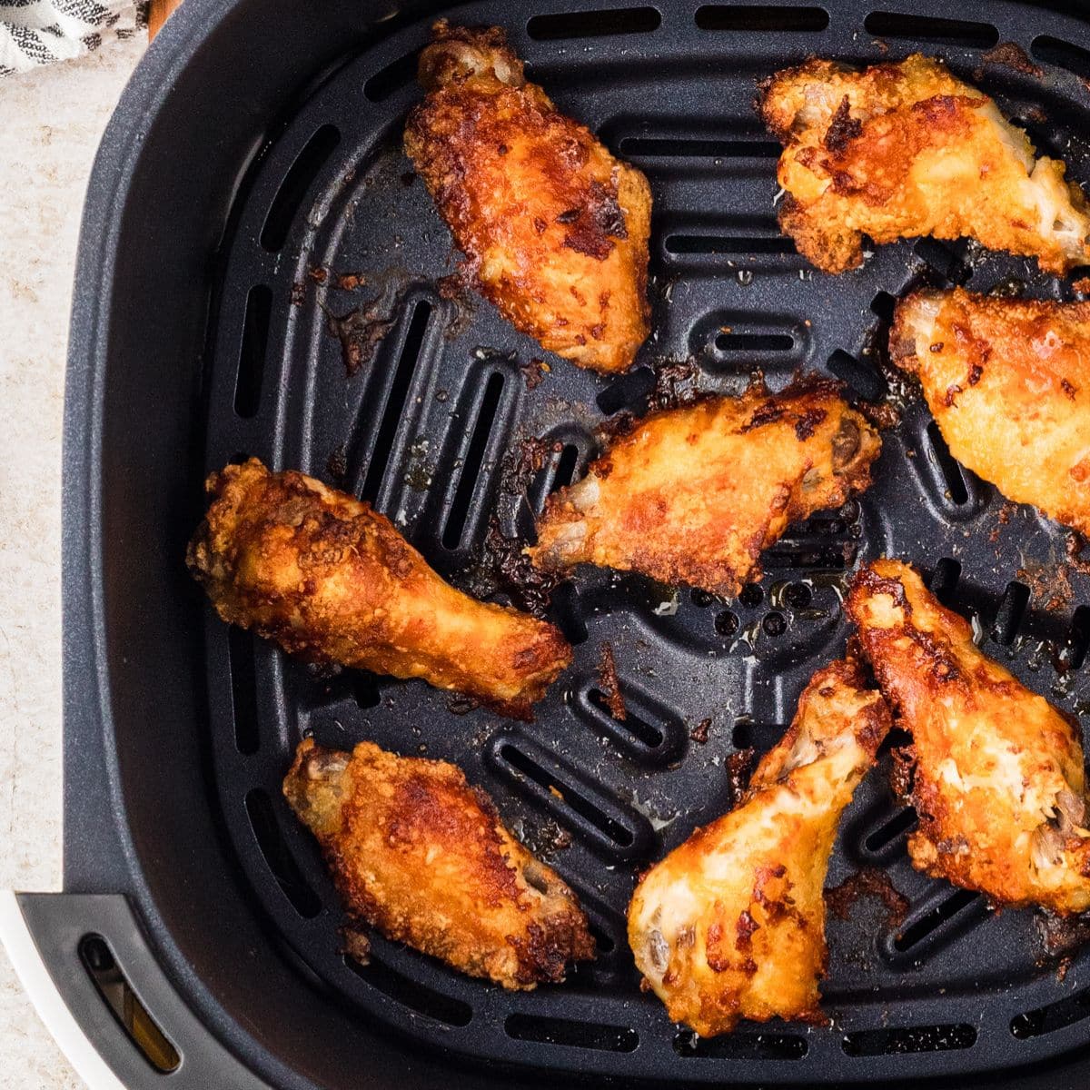 Crispy cooked chicken wings in an air fryer basket on a light countertop.