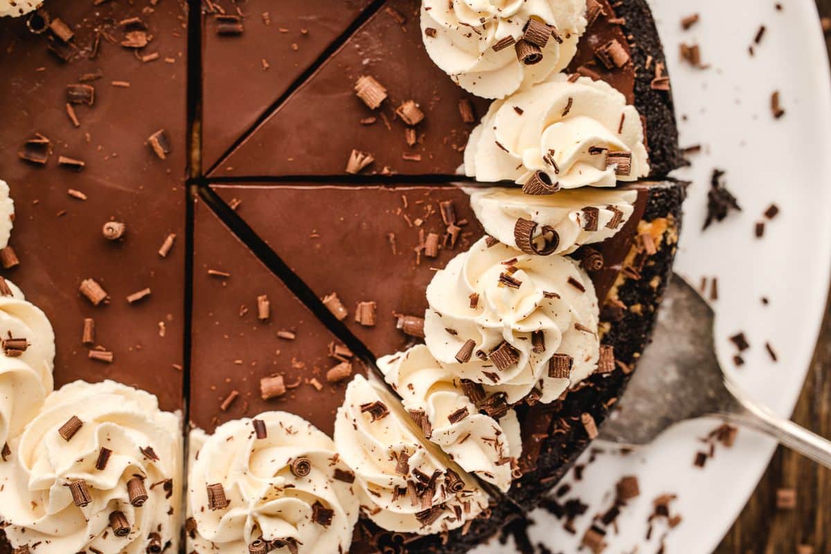 Bailey's cheesecake and chocolate curls, partially sliced on a white plate.