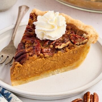 A slice of pecan-topped pumpkin pie with whipped cream on a plate and a fork beside it.