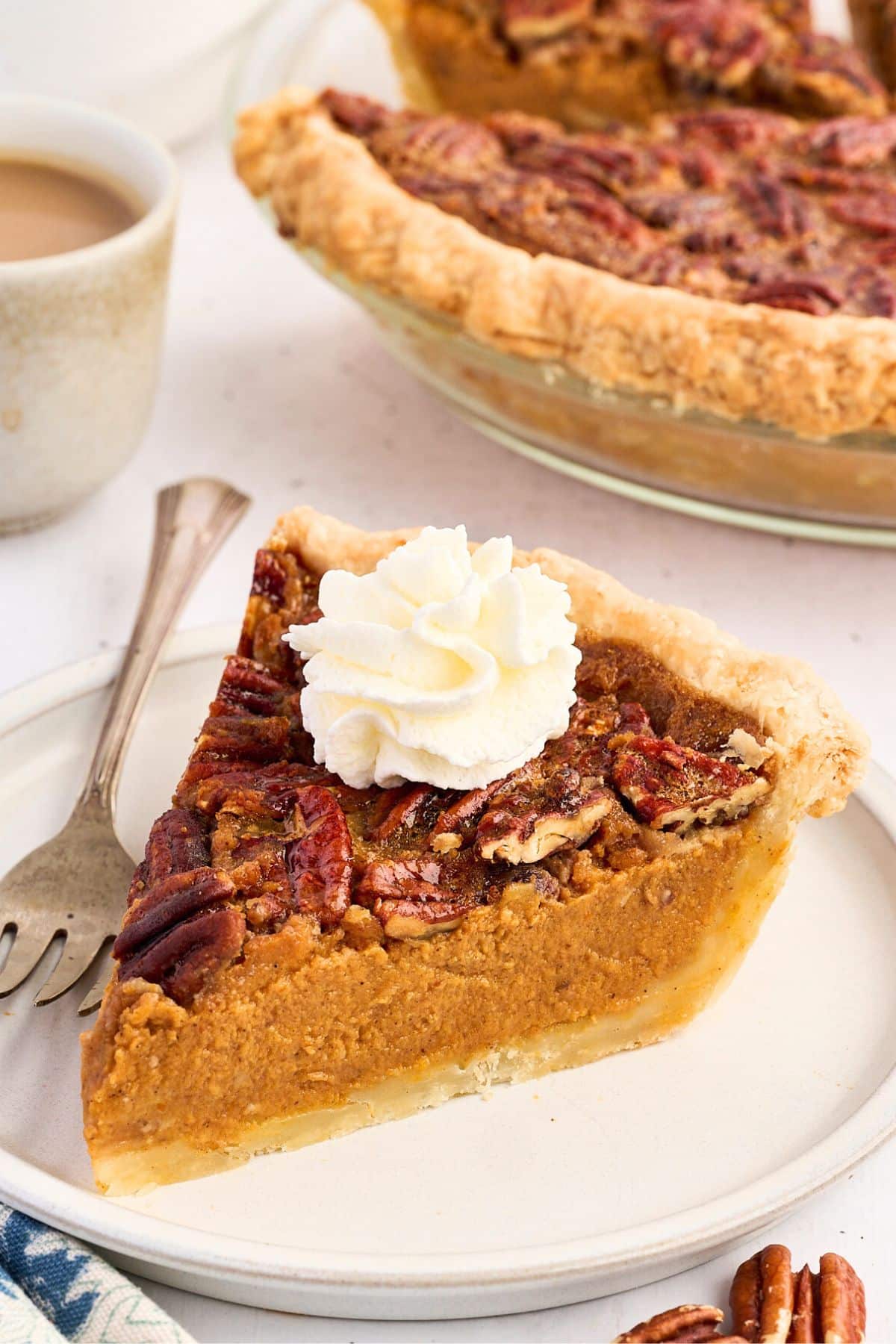 A slice of pecan pie with whipped cream on top, served on a plate with a fork; whole pie in background.