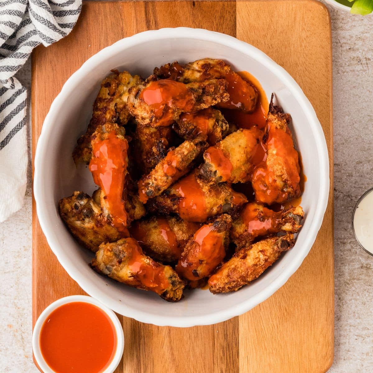 A bowl of crispy chicken wings topped with bright orange buffalo sauce on a wooden board.