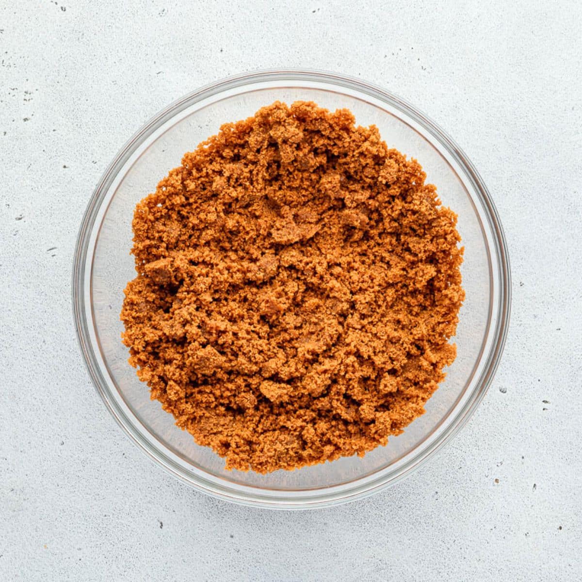 A glass bowl filled with cookie crumbs on a light gray surface.