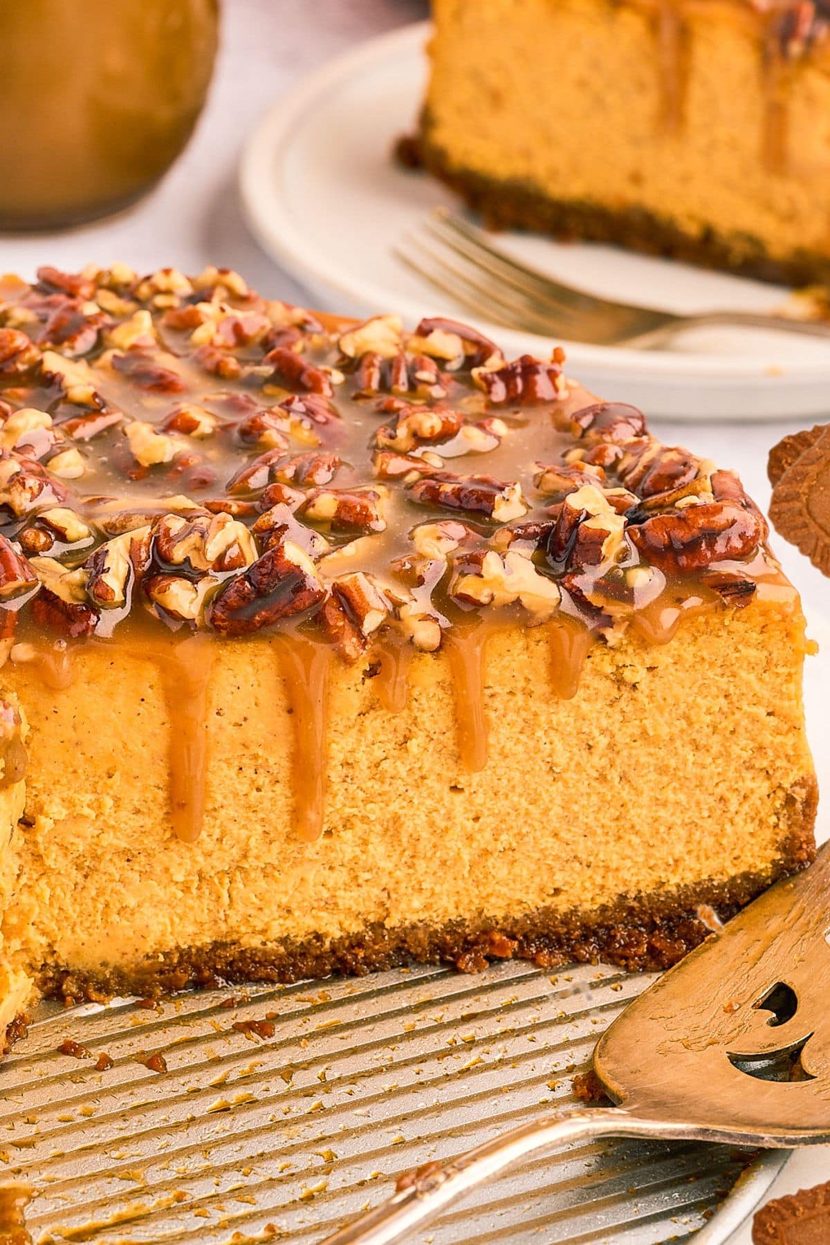 A sliced pumpkin cheesecake topped with caramel and chopped pecans, served on a metal tray.
