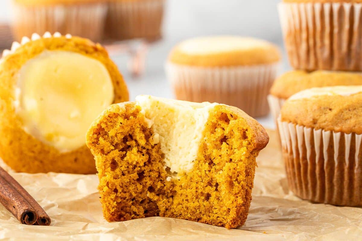 Pumpkin muffin with cream cheese filling, sliced in half, surrounded by whole muffins on parchment paper.