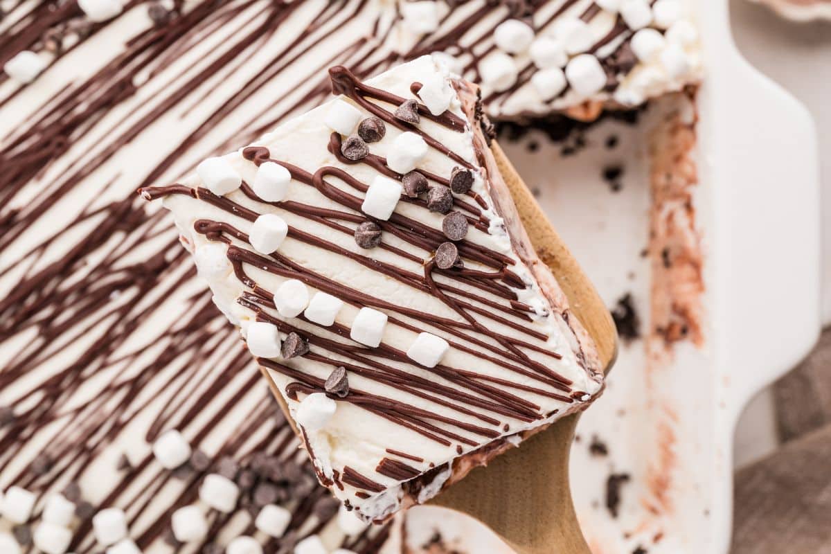 A dessert square topped with chocolate drizzle, mini marshmallows, and chocolate chips on a spatula.