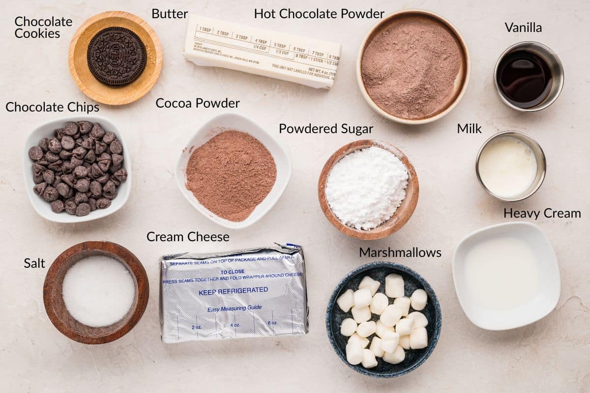 Ingredients for a hot chocolate dessert lasagna arranged on a table, each labeled, including cookies, cocoa, and marshmallows.