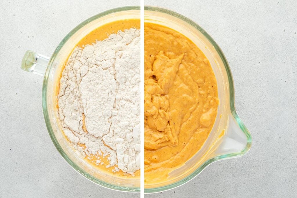 Glass mixing bowl with pumpkin batter, half with flour on top and half fully mixed, on a light surface.