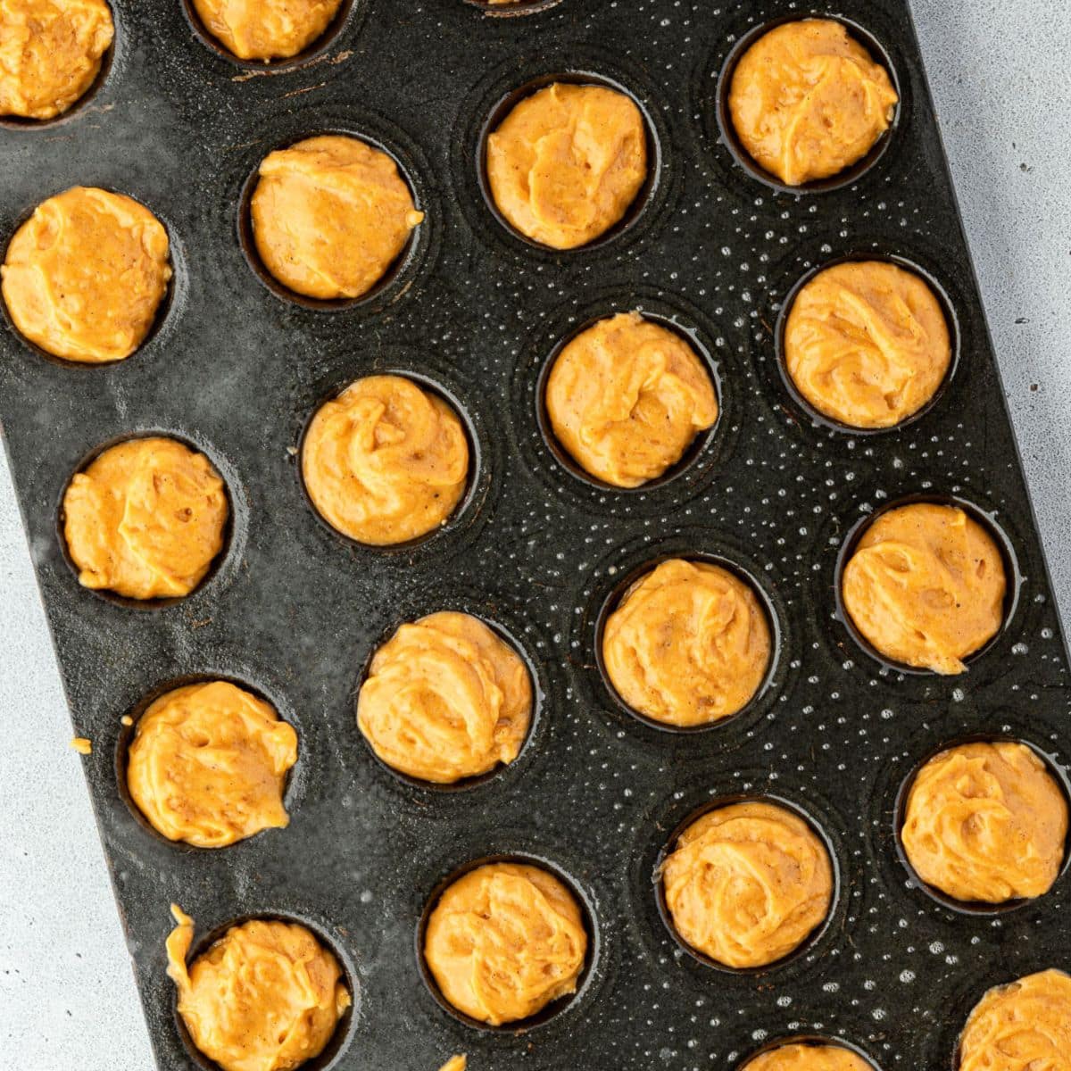 A muffin tin filled with orange batter, ready to be baked, viewed from above.