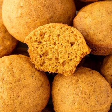 A close-up of round pumpkin cookies, with one cookie broken open to show its soft, fluffy texture inside.