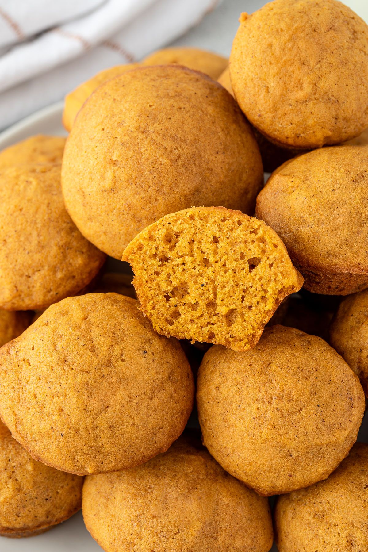A plate of pumpkin cookies, with one cookie broken in half to show its soft, orange interior.