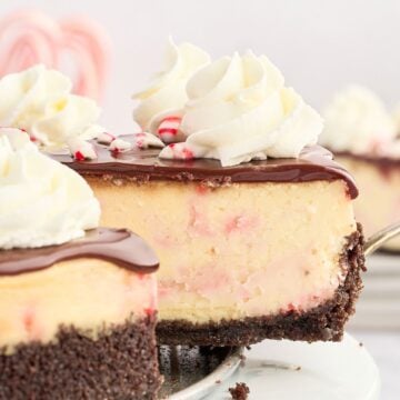 A slice of cheesecake with chocolate crust, chocolate topping, whipped cream, and candy cane pieces.