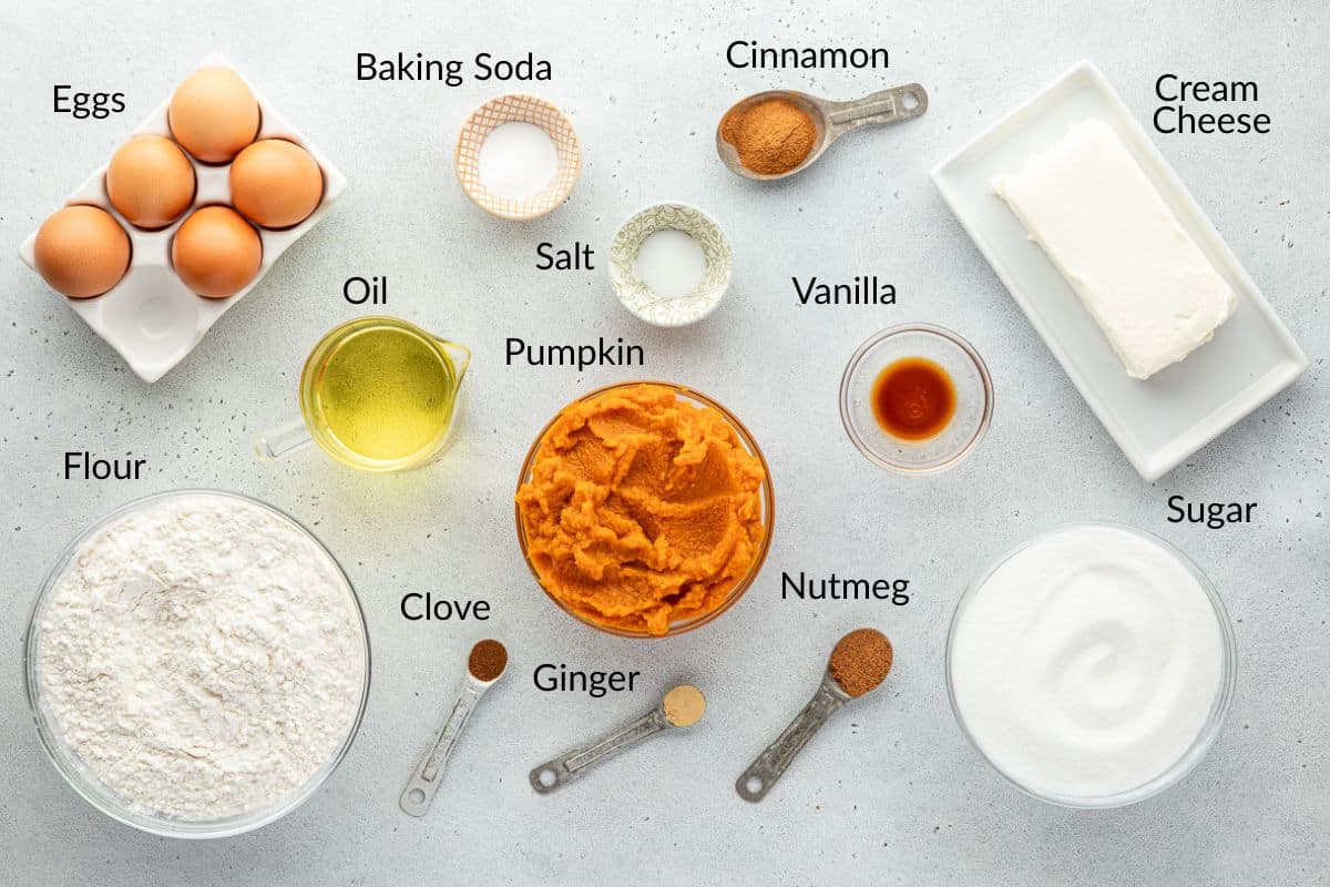 Baking ingredients including eggs, flour, pumpkin, oil, spices, cream cheese, sugar, and vanilla on a table.