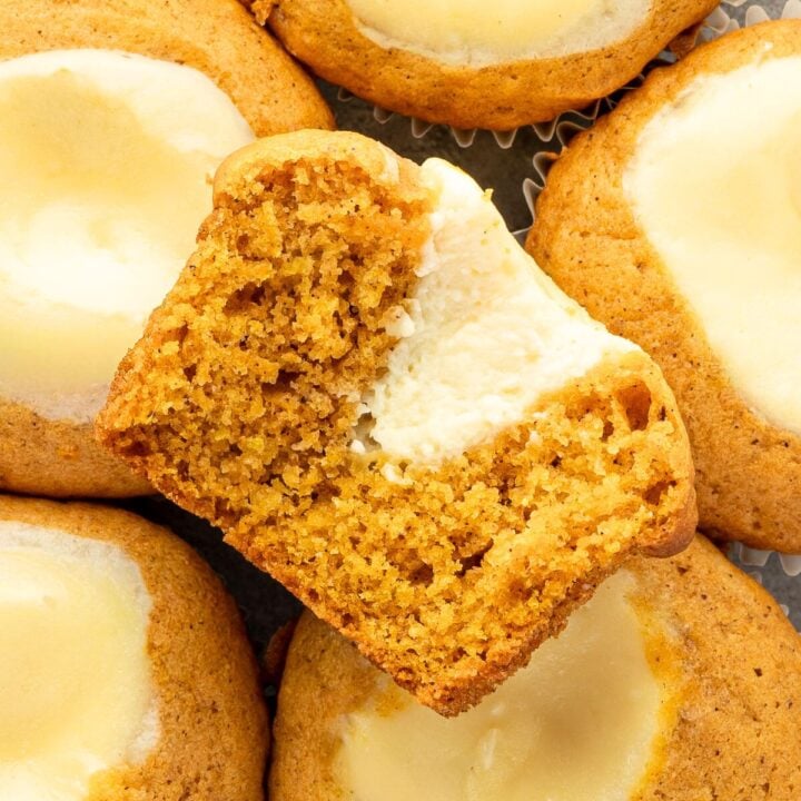 A close-up of pumpkin cookies with cream cheese filling, one cookie is broken in half to show the inside.
