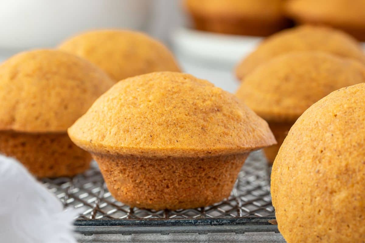 Golden brown pumpkin muffins cooling on a wire rack, with more muffins in the background.
