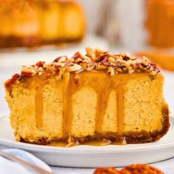 A slice of pumpkin cheesecake with caramel sauce and chopped nuts on top, served on a white plate.