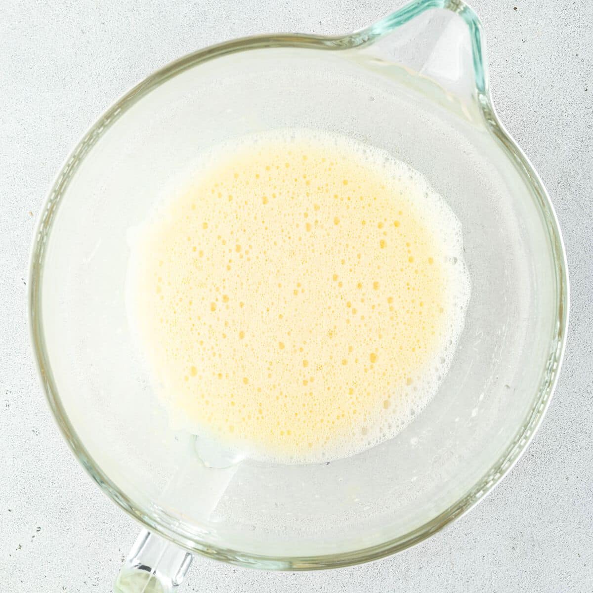 A glass bowl filled with a light yellow, frothy mixture on a gray surface.