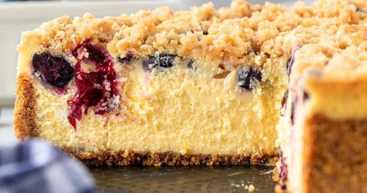 A close-up of a berry cheesecake with a crumbly topping and a thick, creamy filling.