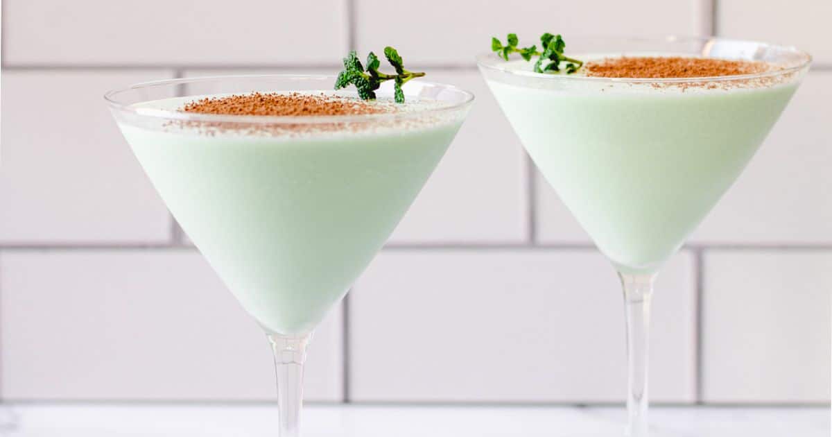 Two mint-green cocktails in martini glasses, topped with cocoa powder and garnished with fresh mint.