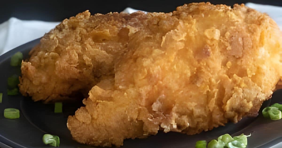 Two pieces of crispy fried chicken on a dark plate, garnished with chopped green onions.