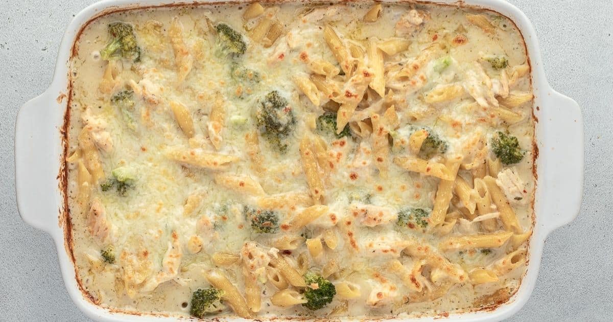 A baked pasta casserole with penne, broccoli, chicken, and melted cheese in a white dish.