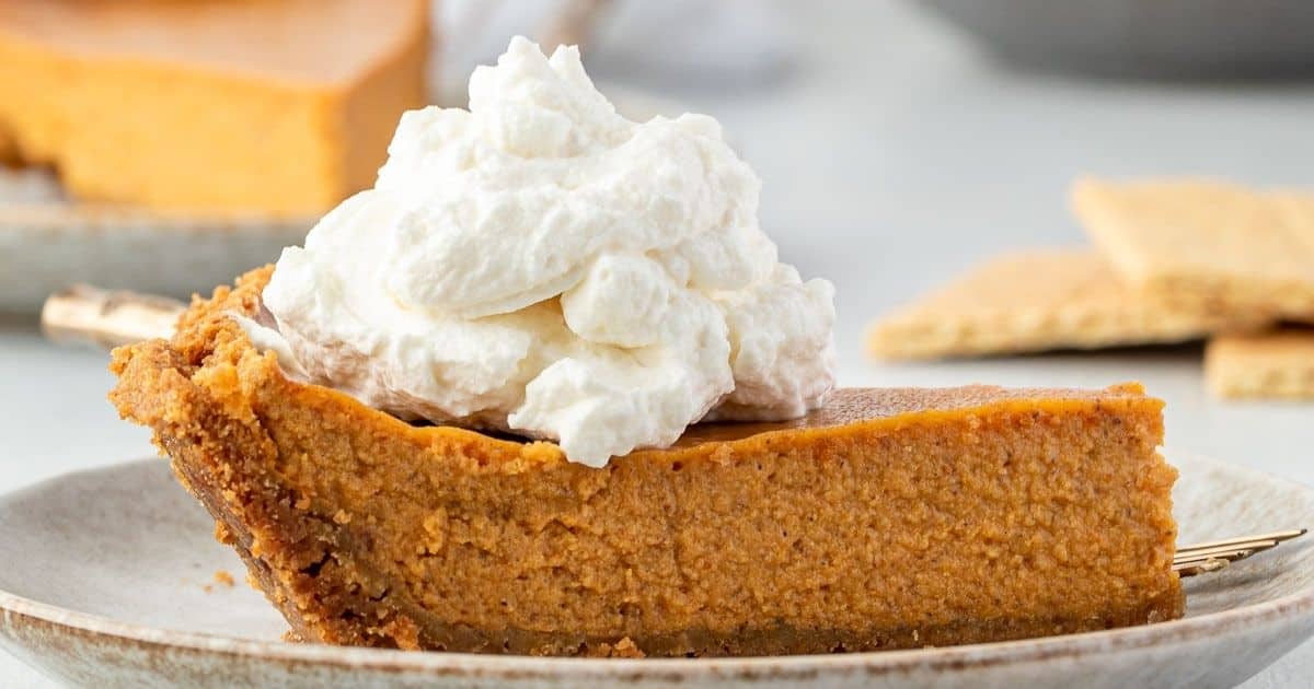 A slice of pumpkin pie topped with whipped cream on a plate.