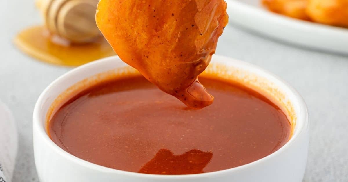 A chicken wing being dipped into a bowl of bright orange buffalo sauce.