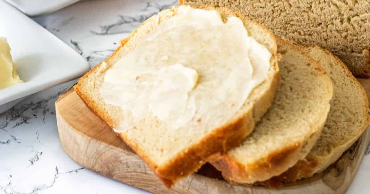 Two slices of bread on a wooden board, one topped with a spread of butter.