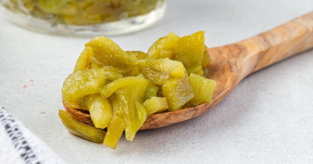 Chopped green chiles on a wooden spoon, with more chiles in a jar in the background.