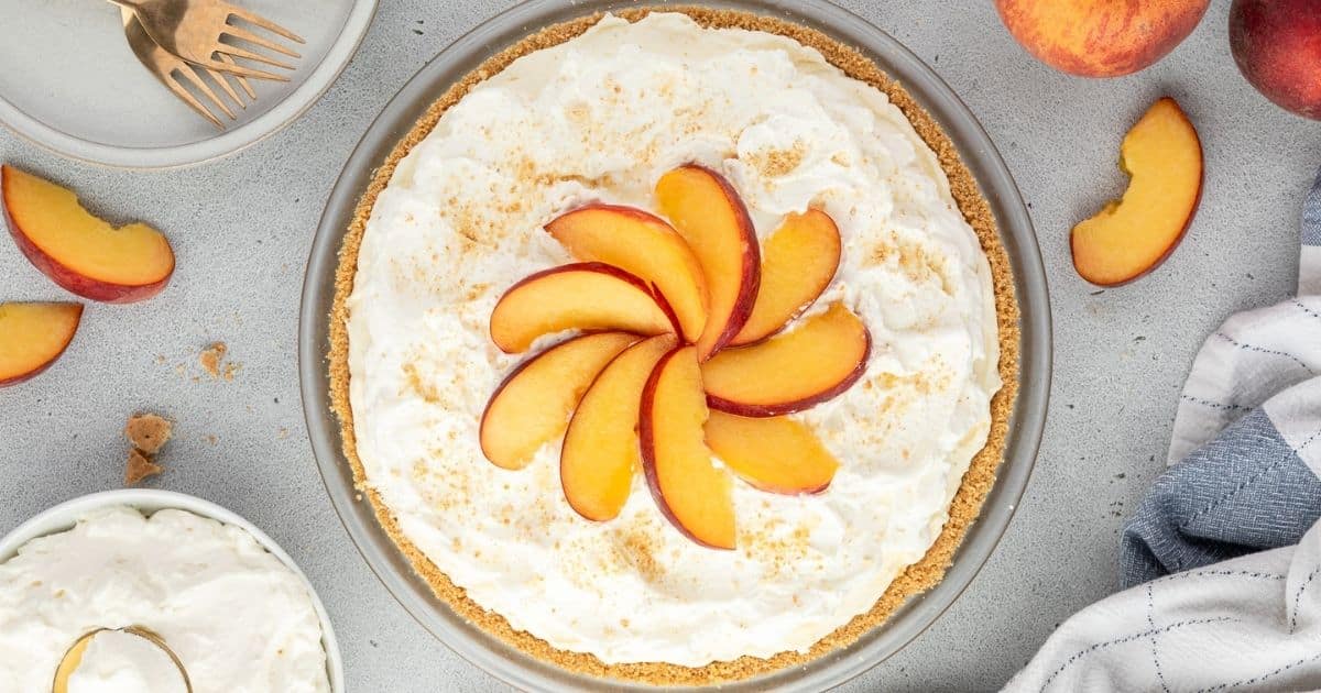 A peach cream pie topped with fresh peach slices arranged in a spiral on a light countertop.