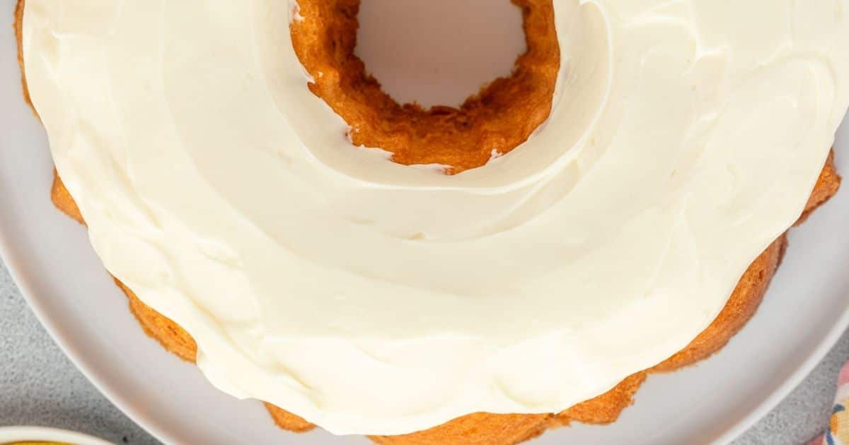 Bundt cake with creamy white frosting on a white plate, viewed from above.