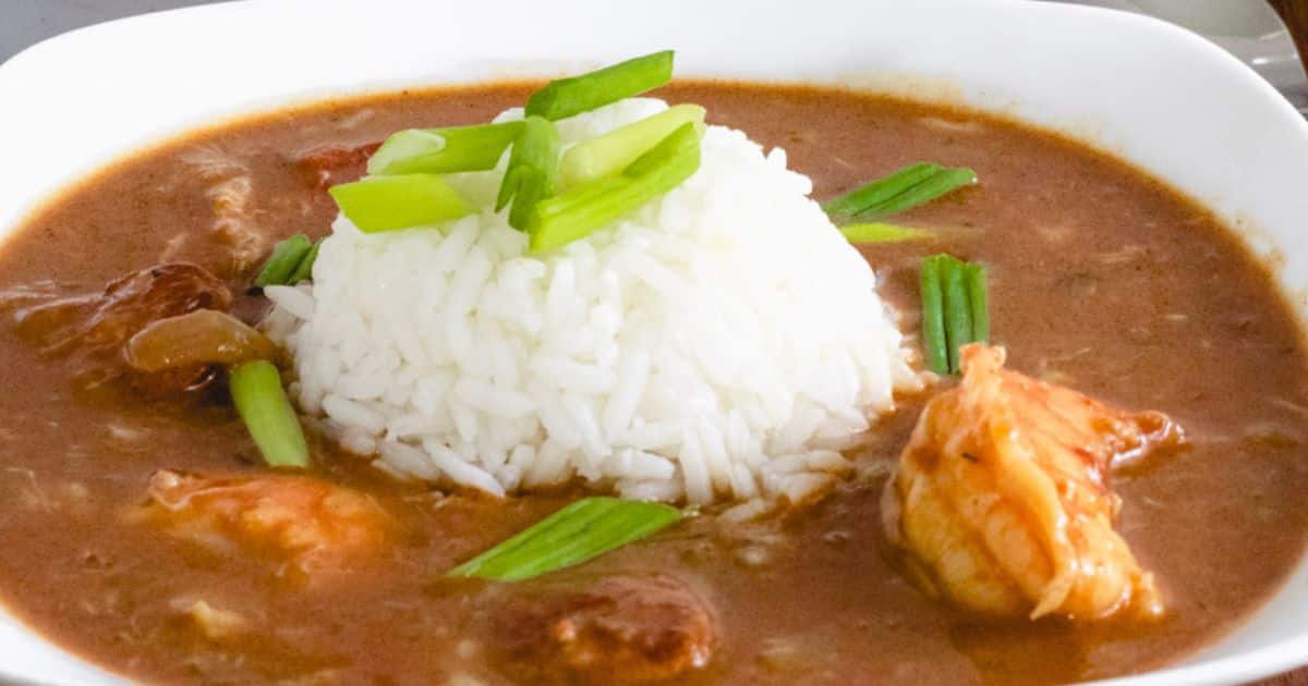 A bowl of gumbo with white rice in the center, garnished with chopped green onions.