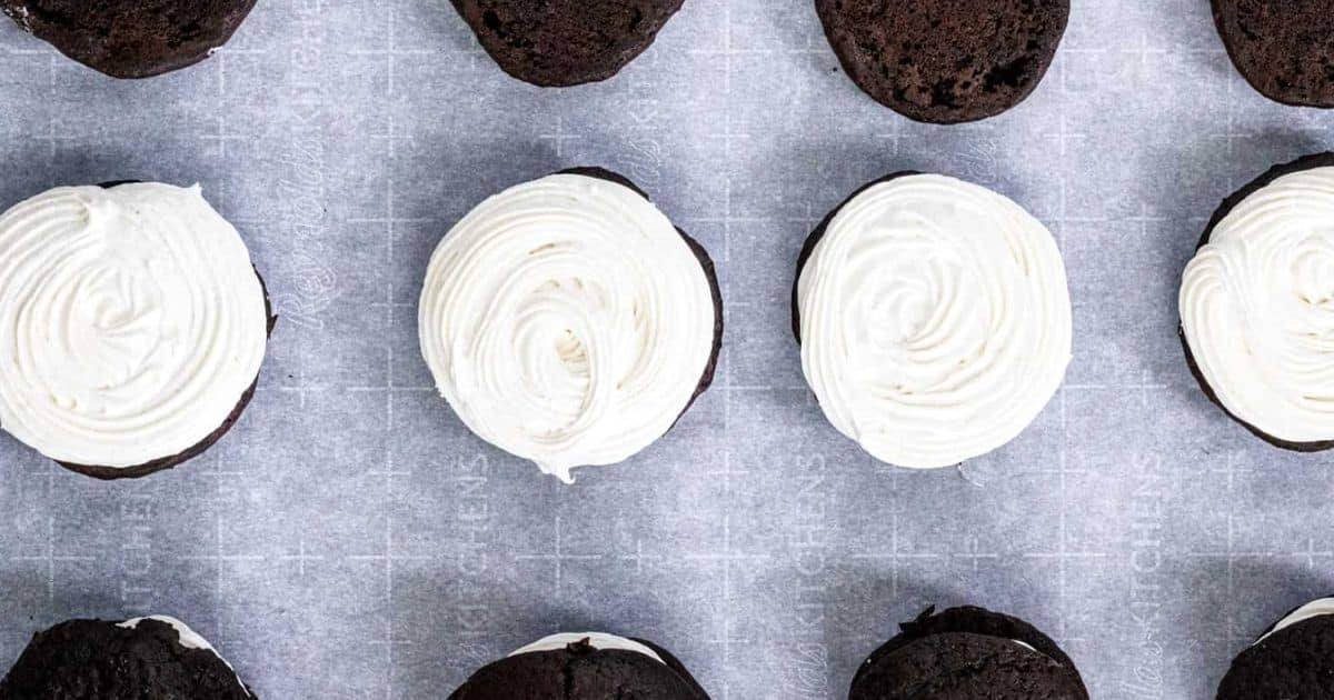 Chocolate cookies topped with swirls of white frosting, arranged neatly on parchment paper.