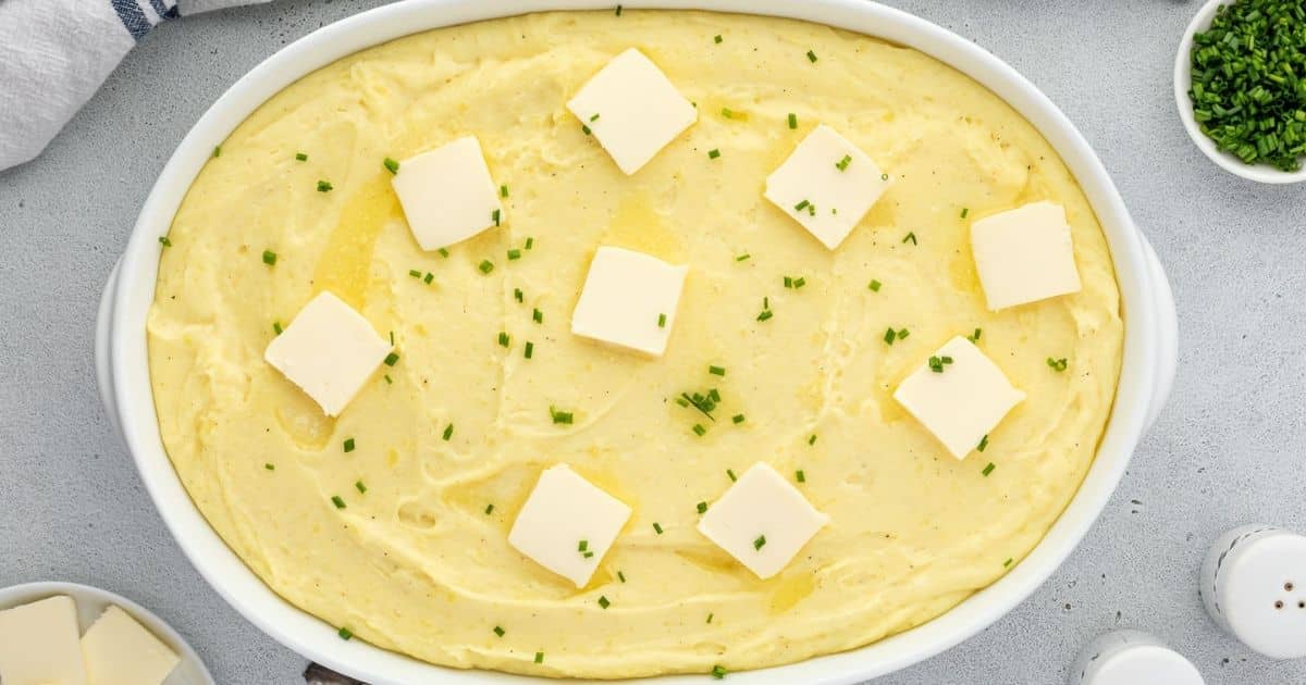 Oval dish of mashed potatoes topped with pats of butter and sprinkled with chopped chives.