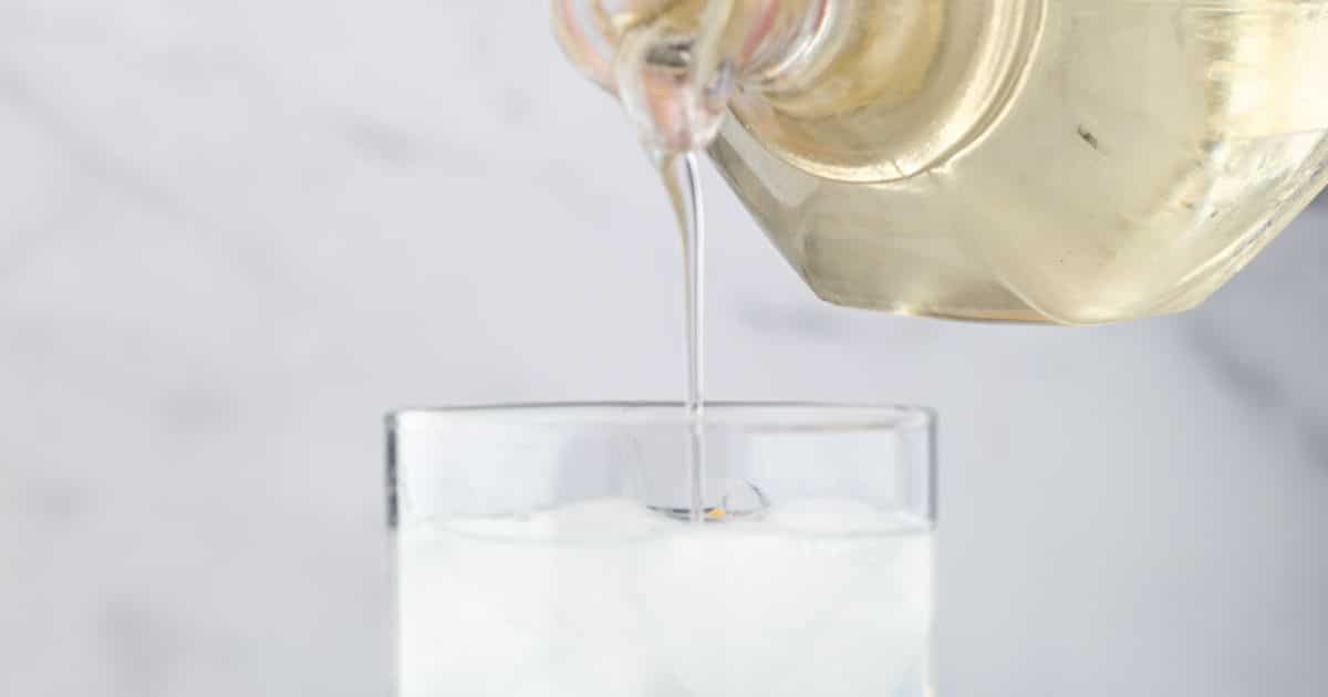 A clear liquid is being poured from a glass pitcher into a glass filled with ice.