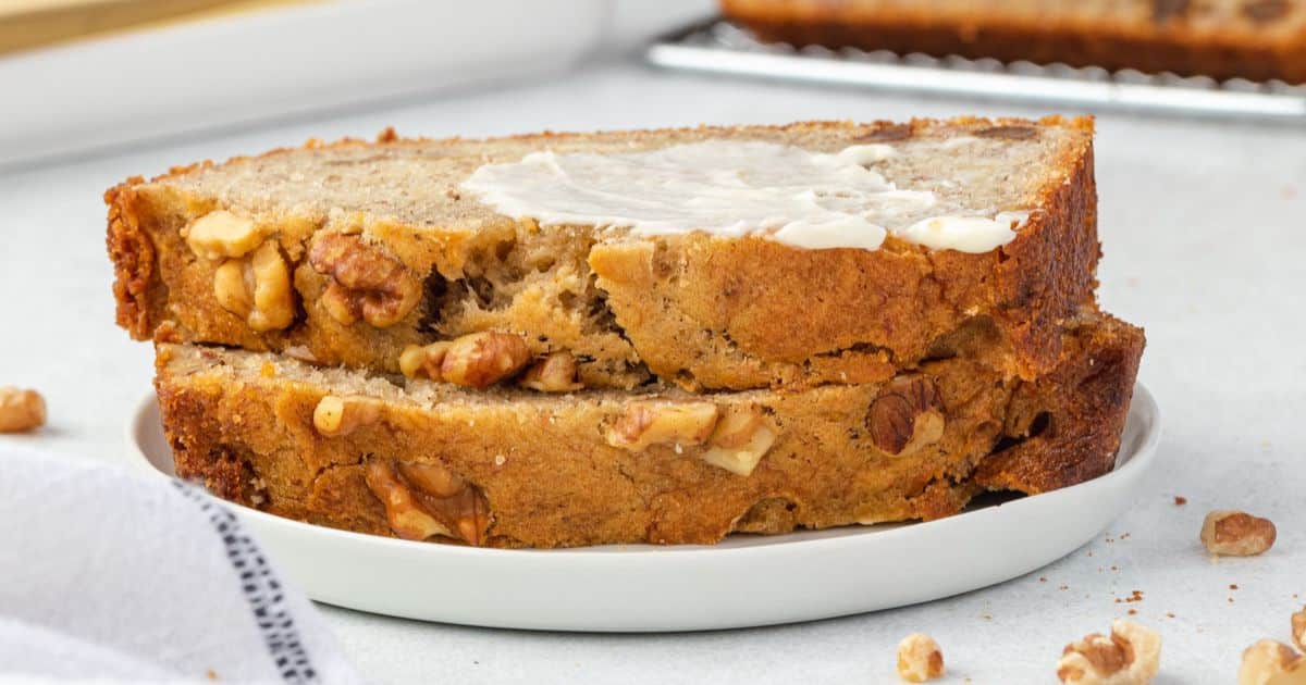 Two slices of walnut banana bread with butter on top, served on a white plate.