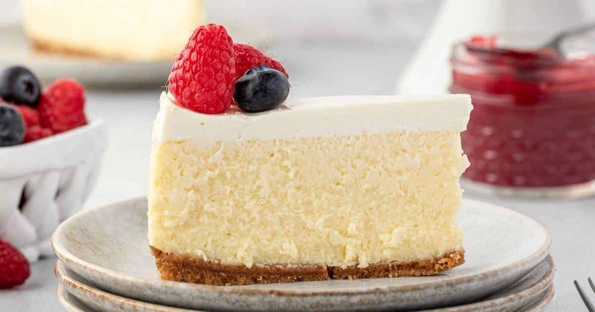 A slice of cheesecake topped with raspberries and a blueberry, served on a plate.