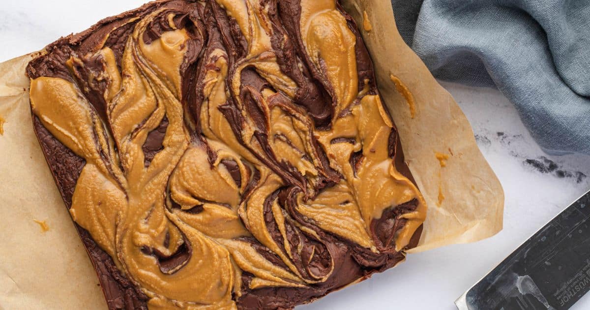 A tray of brownies with a swirled peanut butter topping on parchment paper.