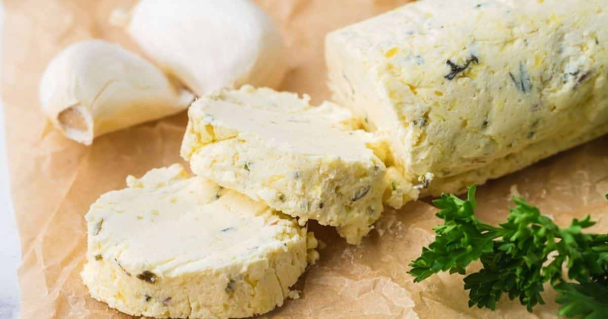 Herb butter slices on parchment paper with garlic cloves and fresh parsley nearby.