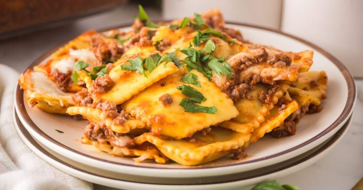 Plate of ravioli topped with meaty tomato sauce and fresh parsley, served on a white dish.