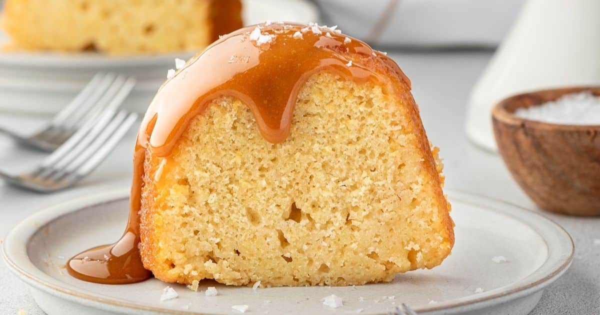 A slice of yellow cake topped with caramel sauce and a sprinkle of salt on a white plate.