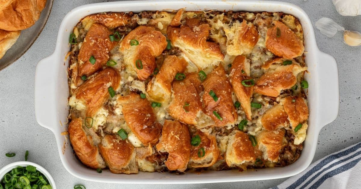 Golden croissant pieces baked with cheese and green onions in a rectangular white casserole dish.